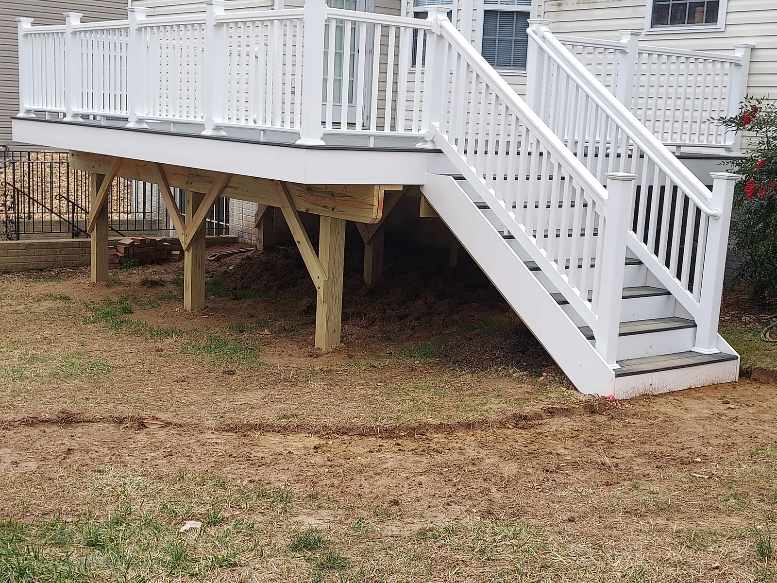 Raised deck with exposed support posts and diagonal framing braces, white railings around the platform, and a staircase with matching railings leading to the yard.