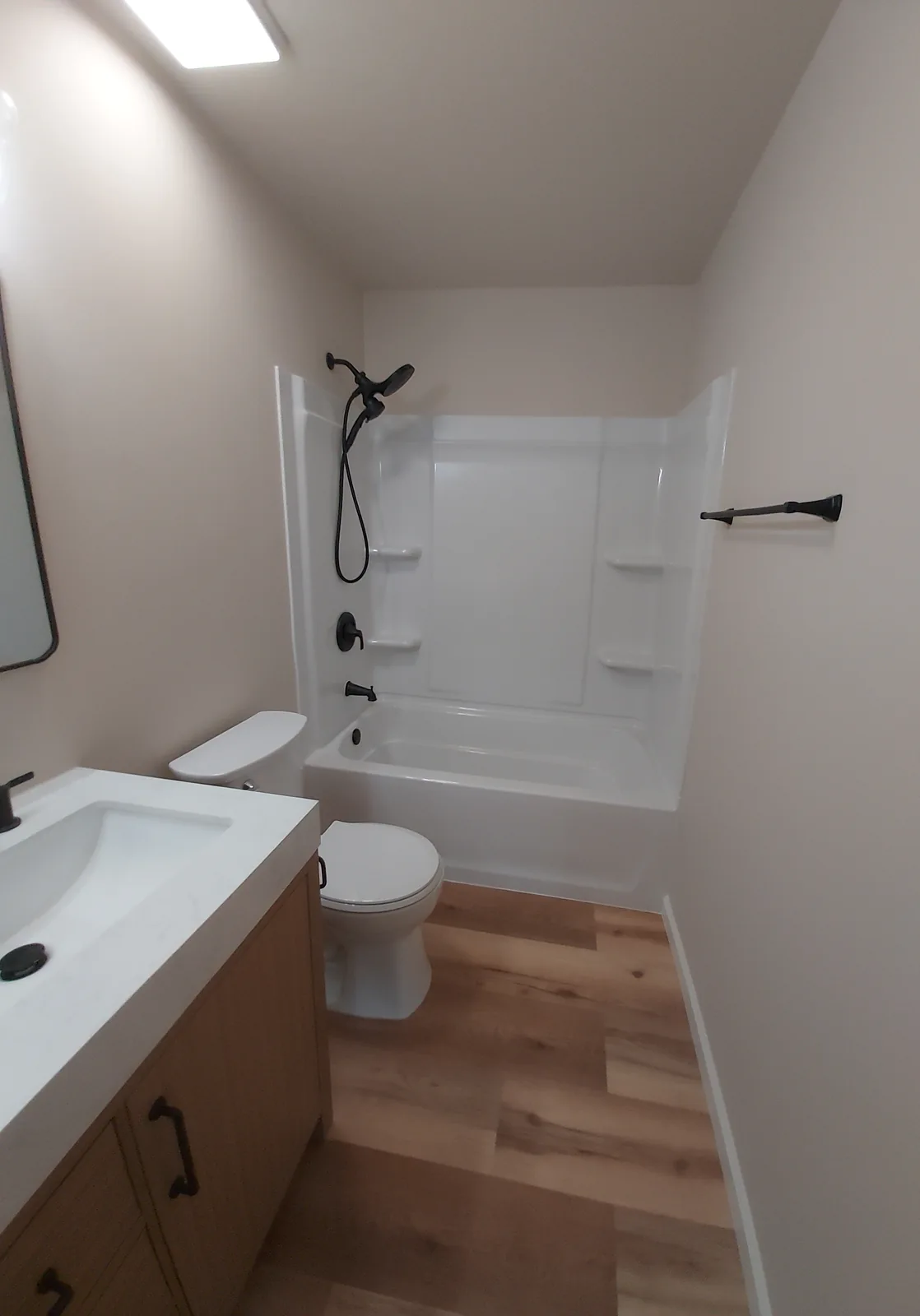 Bathroom with a white bathtub and surround with built in shelves, black shower fixtures, a brown vanity with a white countertop, and a wood patterned floor.